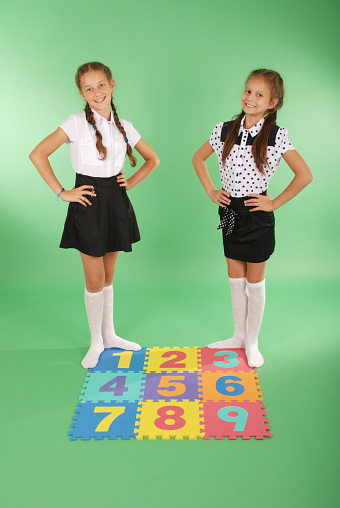 Two girls on rug with numbers one, two, three, four, five, six, seven, eight, nine on green background