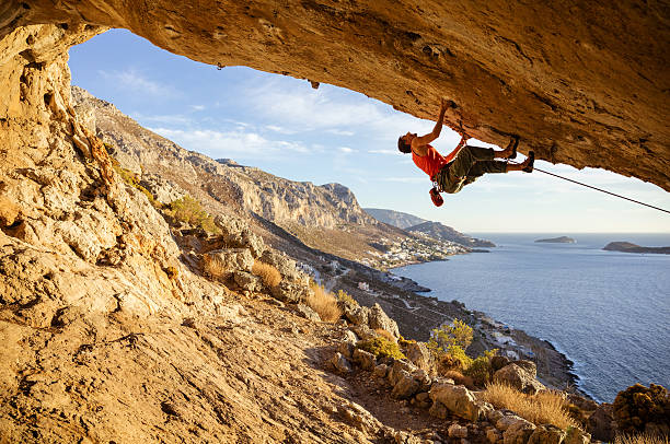 young man climbing in cave - climbing men sea cliff imagens e fotografias de stock