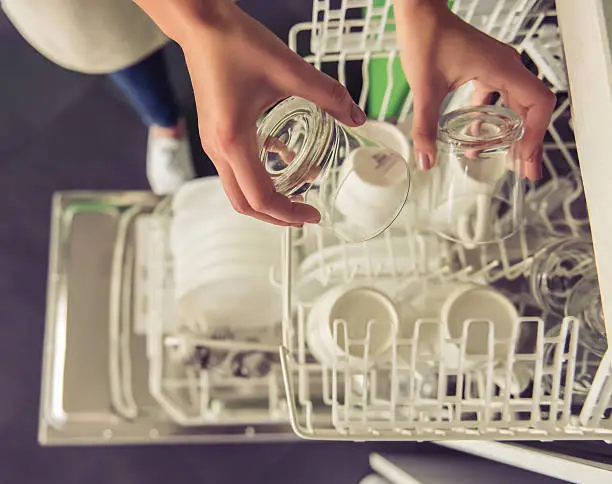 Cropped image of beautiful young woman putting dishes into dishwasher in kitchen