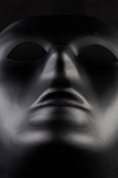 istock Anonymous black mask protruding from pitch black background - he 626350080