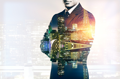 Young man in suit and with folded arms on abstract illuminated night city background. Double exposure