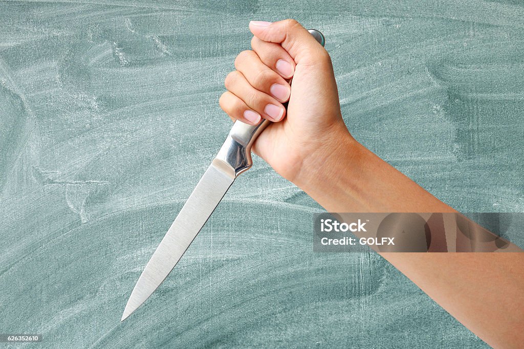 Hand holding a knife Hand holding a knife ready to strike down on green blackboard background Aggression Stock Photo