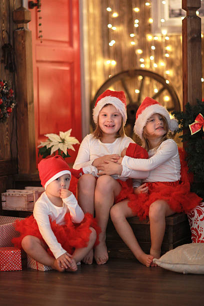 istock Siblings sisters in santa hats with doll near  fireplace 626371328