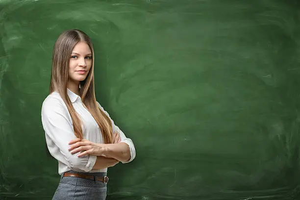 Young businesswoman with his arms across on green chalkboard background. Daily planning. Time-management. Secretary work.