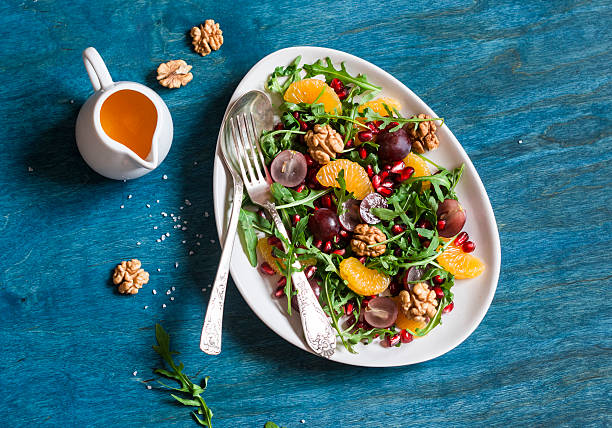 Delicious fruit salad. Grapes, tangerine, pomegranate and arugula fruit salad. On blue wooden background, top view. Flat lay