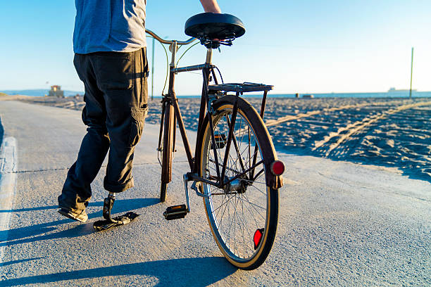 Mid adult male with a prosthetic leg riding a bicycle along the beach front. Los Angeles, America. October 2016