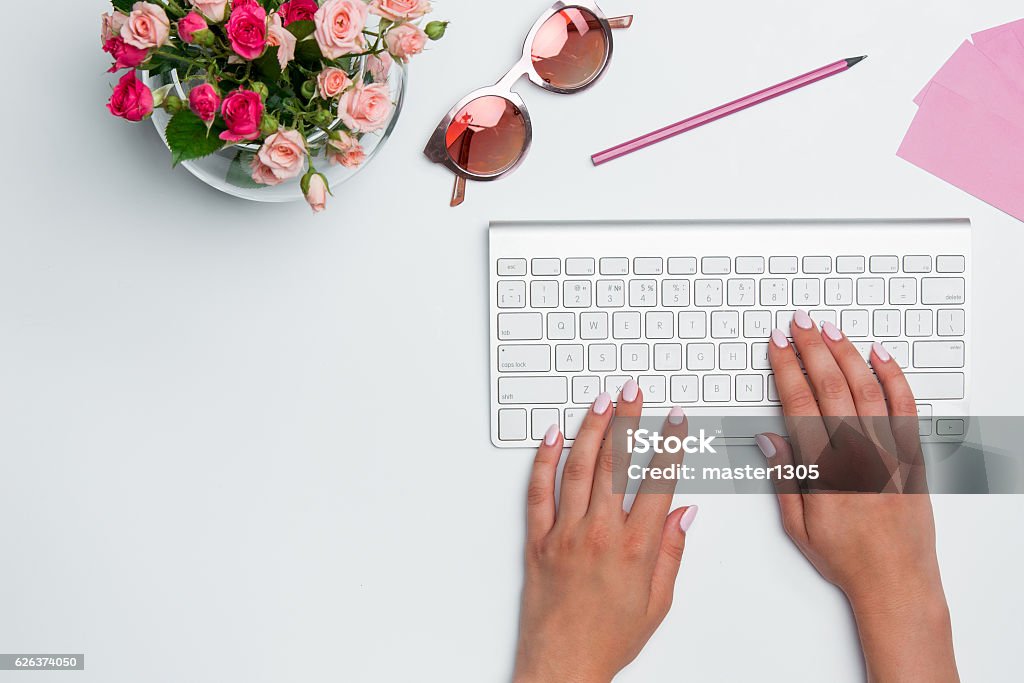 Office desk table with female hands, computer, supplies, flowers Office desk table with female hands, computer, supplies, flowers. Top view with copy space Above Stock Photo
