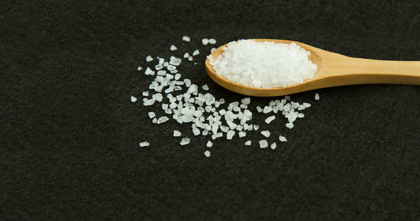 istock Spoon with white stone salt on the black background 626387512