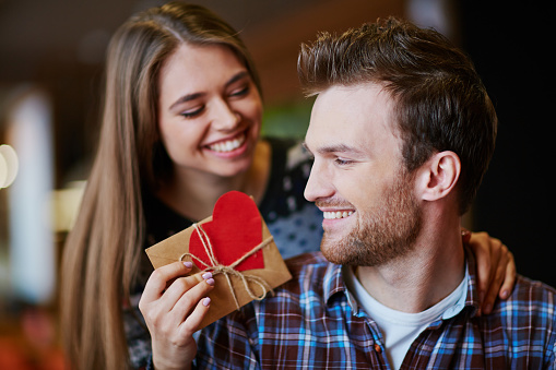Smiling man looking at small present held by his girlfriend