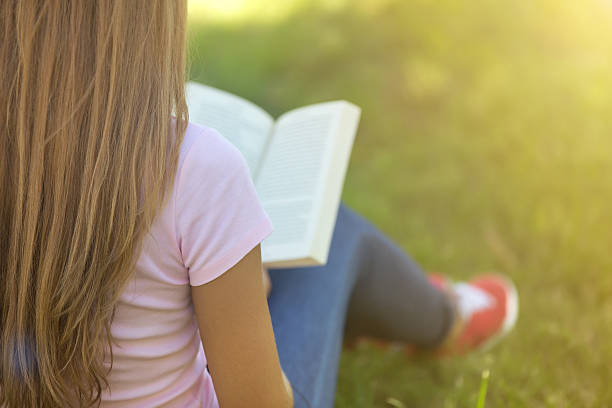 istock Young woman sitting on a grass with book 626411088
