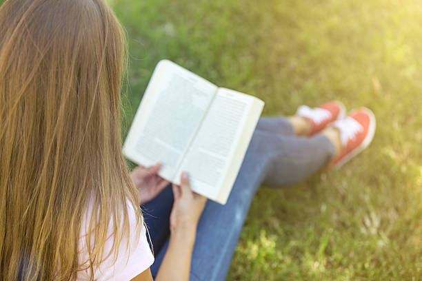 istock Young woman reading book on the grass 626411300