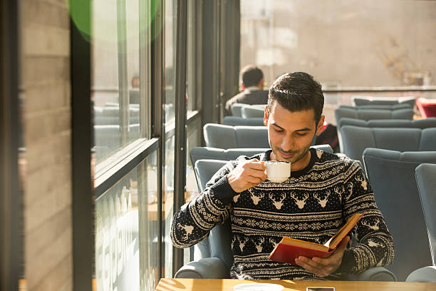 istock Smiling hipster man reading book at cafe 626411380