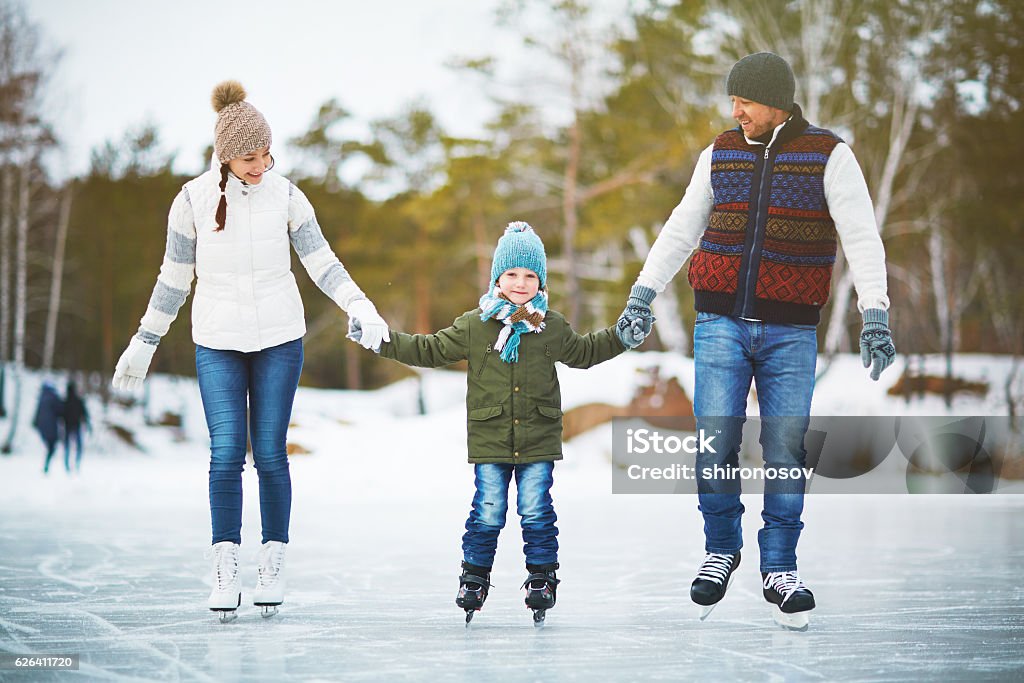 Joyful family of skaters Family portrait of cheerful young parents looking at their son with smile and holding his hands while skating on winter park rink, blurred background Ice-skating Stock Photo