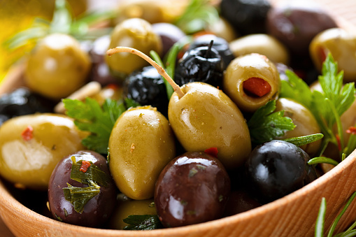 Closeup shot of marinated olives in wooden plate.