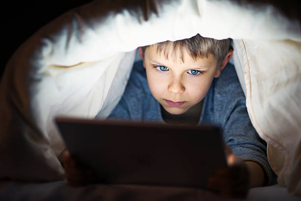 istock Little boy reading book on digital tablet at night 626416132