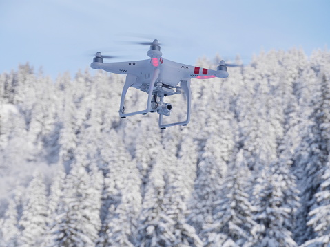 A drone flying high above a forest covered with fresh snow in a bright sunny winter day.