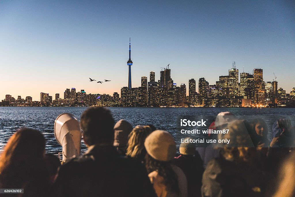 Tourists on a ferry boat in Toronto Toronto, Canada - October 13, 2016: People on the ferry boat from Toronto islands to downtown looking at the skyline and taking pictures with phones at sunset People Stock Photo