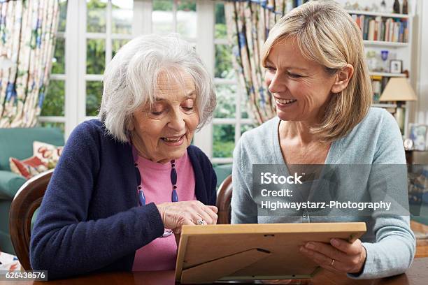 Senior Woman Looks At Photo In Frame With Mature Stock Photo - Download Image Now - Picture Frame, Care, Memories