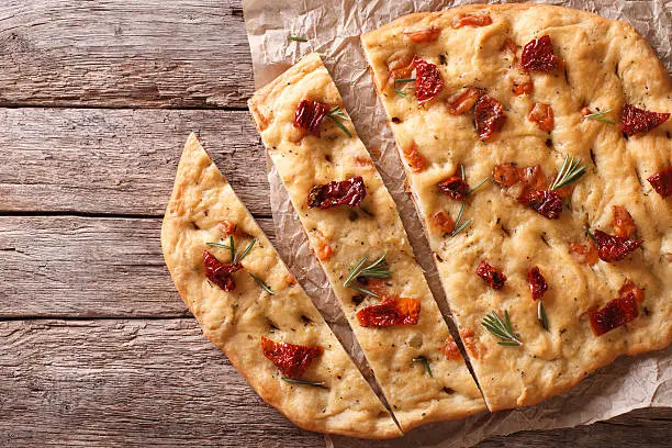 Sliced bread Italian focaccia with sun-dried tomatoes and rosemary on the table. horizontal view from above