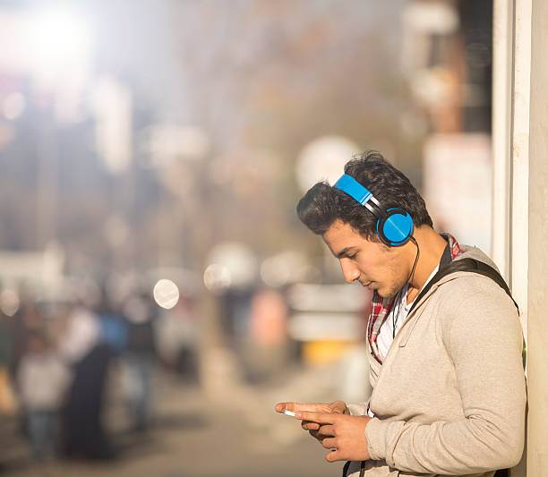 Man sitting near the city river  listen to music on headset and relaxing on beautiful day.