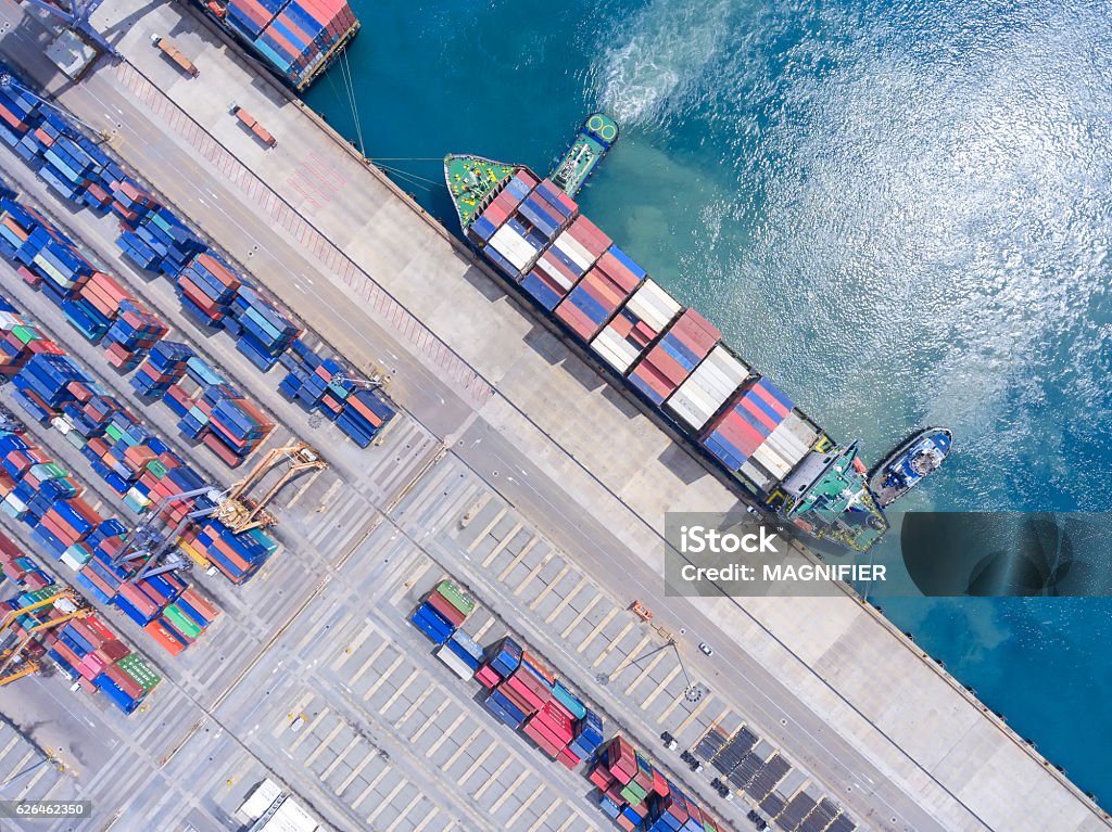container ship in import export and business logistic.By crane , container ship in import export and business logistic.By crane , Trade Port , Shipping.Tugboat assisting cargo to harbor.Aerial view. Cargo Container Stock Photo
