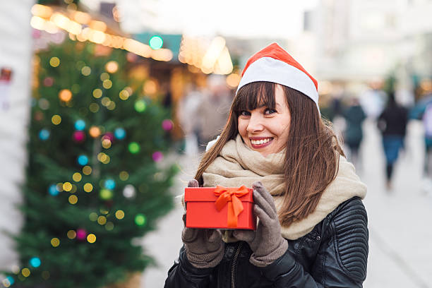istock beautiful woman in santa hat holding present box 626487720
