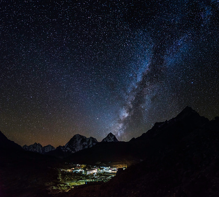 Stars and Milky Way shining over the warmly illuminated Sherpa village of Lobuche, overlooked by the snow capped peaks of the remote Himalaya mountains deep in the Everest National Park of Nepal.