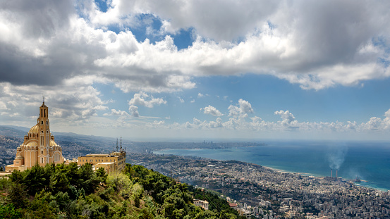 The photo taken on a partially cloudy stormy day concentrates in the foreground on the Harissa monastery and depicts in the background the coastline of the city of Beirut.