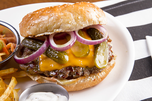 Fresh, tasty and delicious beef hamburger with French fries, tomato and pepper red salsa, Spanish onion, garlic, egg and green pepper, served  on a plate, bar, restaurant or home kitchen table, close up view with copy space, representing fast food and city life, indulgence and joy through gourmet lifestyle