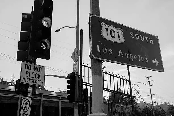 A black and white photograph of a Los Angeles, California 101 Freeway Sign and Stoplight with barbed wire in the background.