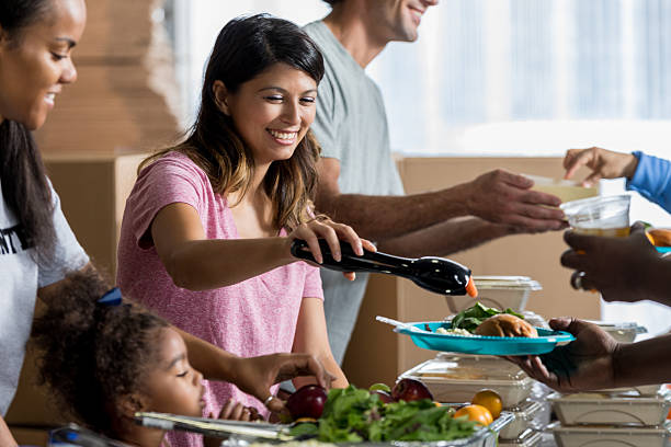 Beautiful Hispanic woman serves a meal in soup kitchen Confident Hispanic woman serves healthy meals in a soup kitchen. She is volunteering with her friends and family. soup kitchen stock pictures, royalty-free photos & images