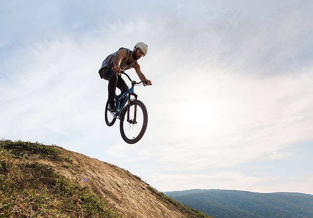 Below view of extreme cyclist doing straight air jump. Low angle view of skillful mountain bike rider jumping over dirt hill against the sky. Copy space. x games stock pictures, royalty-free photos & images