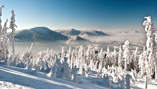 panorama of winter Moravskoslezske Beskydy mountains with Knegyne, Velka Stolova, Radhost and other hills, trees covered by snow and clear sky during hiking to Lysa hora hill