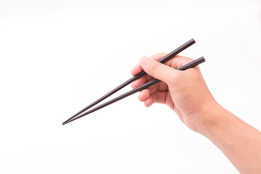 Hand with chopsticks holding salmon maki sushi roll on a blue background. Brightly lit studio shot.
