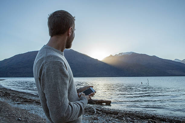 istock Young man by the lakeshore text messages on mobile phone 626586048