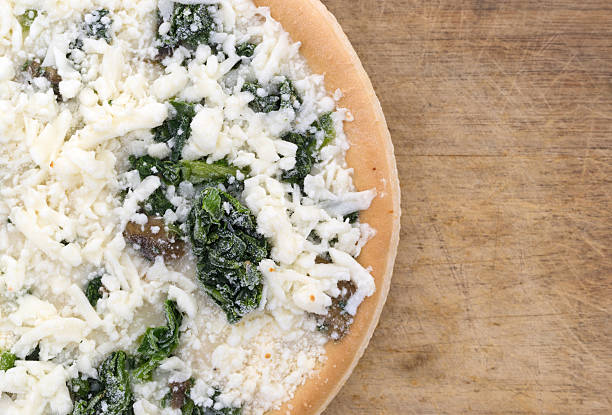 Top close view of a frozen spinach mushroom pizza on a wood cutting board.