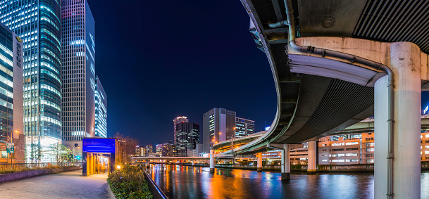 Elevated highway soaring over the tranquil waters of the Kyū-Yodo River reflecting the colourful neon lights of the crowded skyscraper cityscape of downtown Osaka, Japan's vibrant second city.