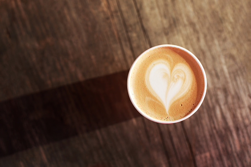 Cup of coffee to go on the wooden table with latte art. Street coffee. Top View.