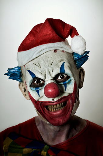 a scary evil clown wearing a santa hat with his mouth open showing his rotten teeth staring at the observer