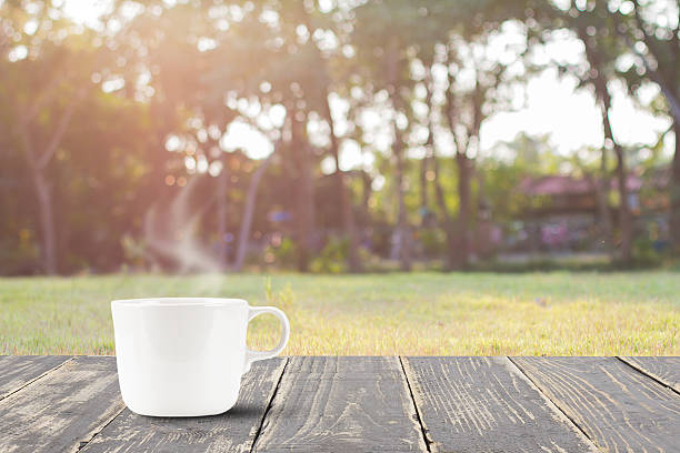 Hot coffee with smoke on vintage wooden table top on blurred meadow and tree  with flare background