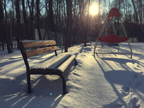 Wooden bench covered with snow at sunset