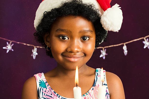 Close up face shot of little afro american girl with christmas hat holding candles.