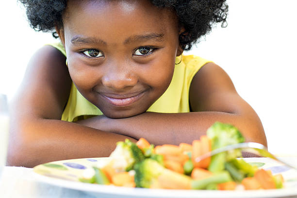 African girl in front of vegetable dish. Close up face shot of cute African girl in front of healthy vegetable dish. Isolated on white. little black girl hairstyle stock pictures, royalty-free photos & images