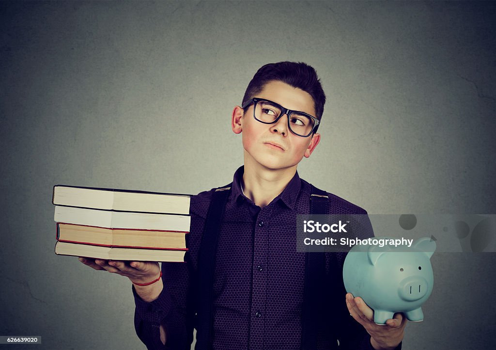 Student loan debt. Man with books piggy bank Student loan concept. Young man with stack pile of books and piggy bank full of debt rethinking future career path Book Stock Photo