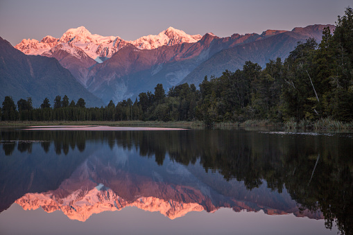 Lake Matheson at sunset, New Zealand's South Island, and the Southern Alps reflection in the mirror-like surface of the lake. Mount Cook and Mount Fox snowcapped peaks on the background.