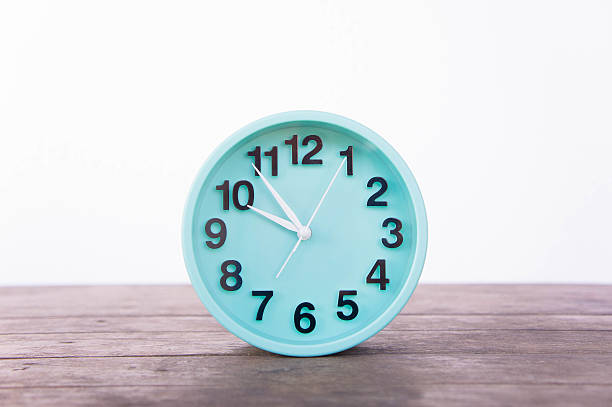 istock Green clock on a wooden table on a white background. 626643708