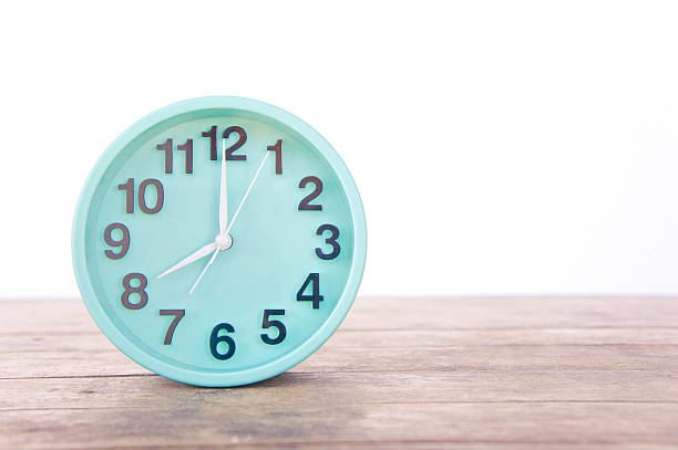 istock Green clock on a wooden table on a white background. 626643716