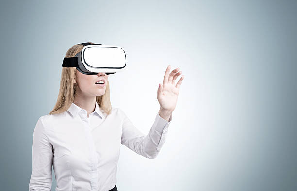 Blond woman in vr glasses near a gray wall Blond woman in virtual reality glasses is standing near a blank gray wall. Concept of hi tech. Mock up head mounted display stock pictures, royalty-free photos & images