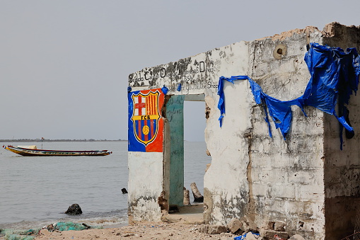 Diogue island, Senegal-April 15, 2014: The ruins of a deserted shop on the shore facing the mouth of the Casamance river still show traces of decoration -crest of Barcelona F.C.- and facade titles.