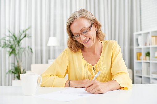 Smiling pretty mature woman writing a letter